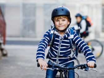 Two school kid boys in safety helmet riding with bike in the city with backpacks. Happy children in colorful clothes biking on bicycles on way to school. Safe way for kids outdoors to school.